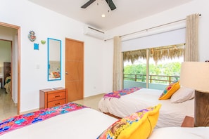 A bedroom with two beds, a wooden wardrobe, a mirror, and a window with a view of greenery.
