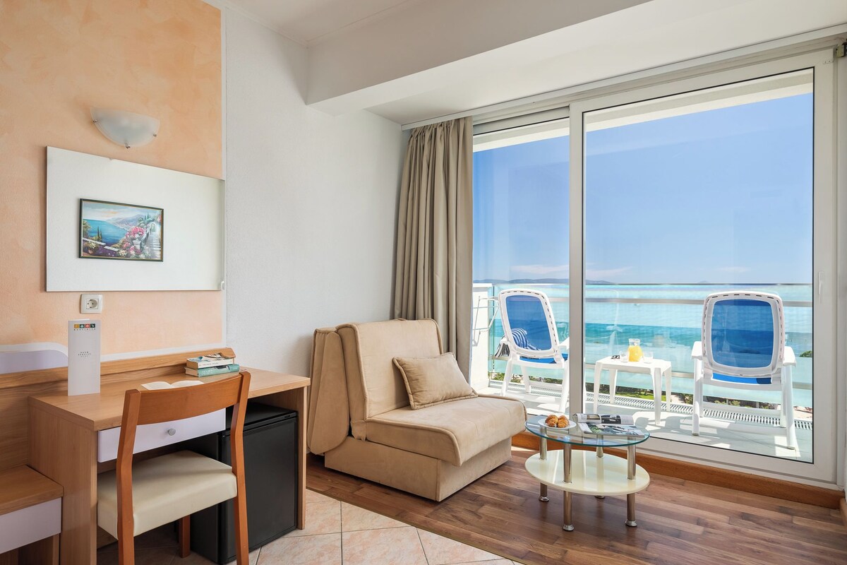 A room with a desk, a sofa, a small table, and a view of the ocean.