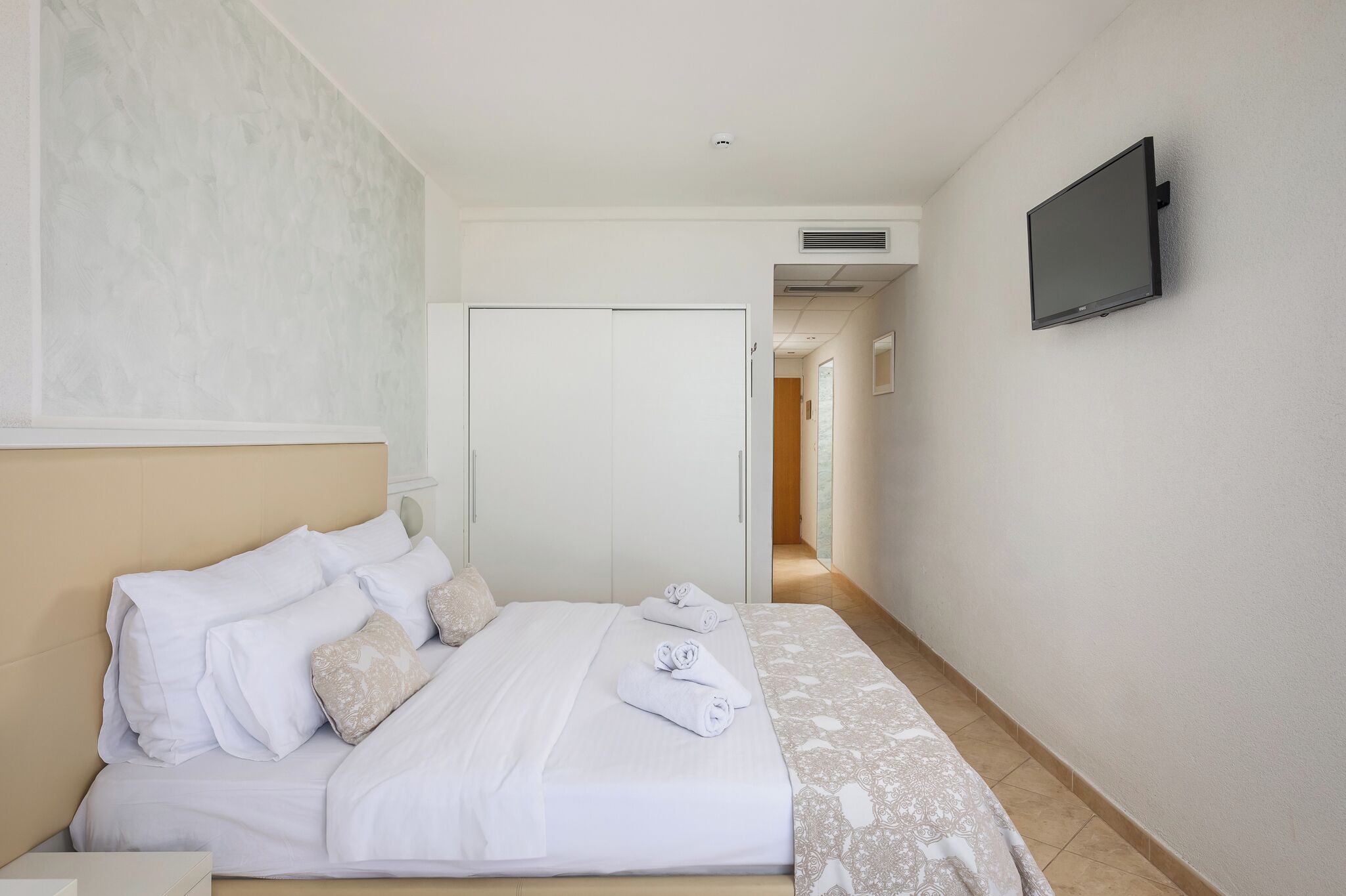 Une chambre d’hôtel comprenant un lit, un téléviseur fixé au mur, une armoire et une porte donnant sur une autre pièce.