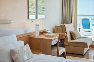 Habitación de hotel con un escritorio de madera, un sofá color beige, una silla, una bañera y vista al mar.
