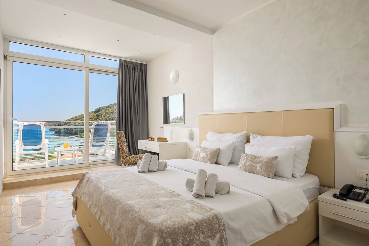 A hotel room with a bed, bedside table, and a view of a pool and mountains.