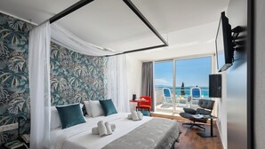A hotel room with a bed, a balcony with a view of the sea, a TV mounted on the wall, and a small table with a chair. - MASLINICA Mimosa Lido Palace Hotel (Labin)