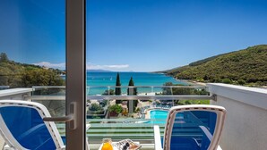 A balcony with a view of a swimming pool, a beach, and a mountainous landscape. - MASLINICA Mimosa Lido Palace Hotel (Labin)