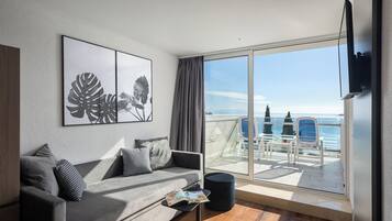 Uma sala de estar moderna com um sofá cinzento, uma mesa de centro e uma janela grande com vista para uma varanda e o mar.