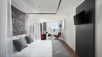 A hotel room with a bed, a desk, a chair, a TV, and a view of the sea.