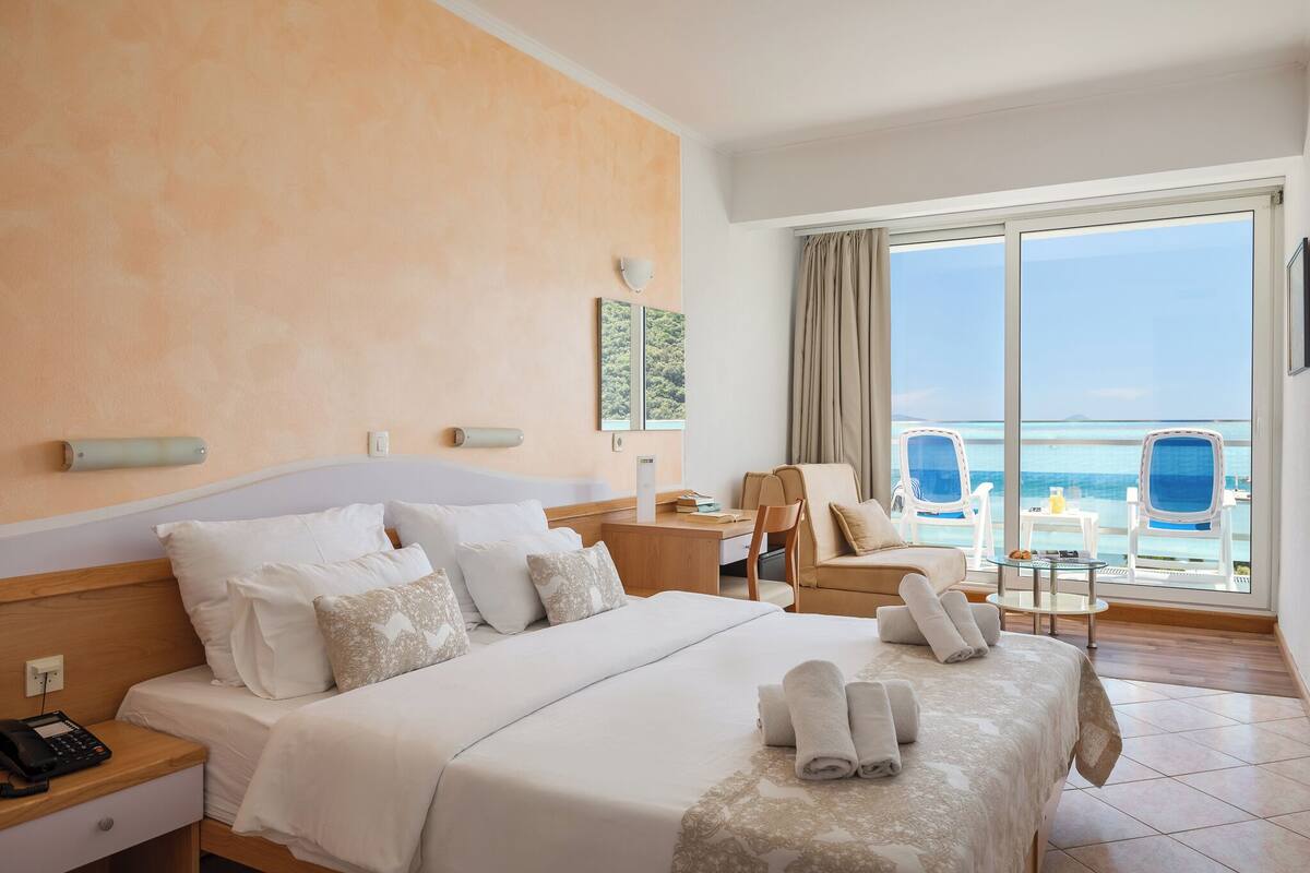 A hotel room with a large bed, a desk, a chair, and a view of the sea.