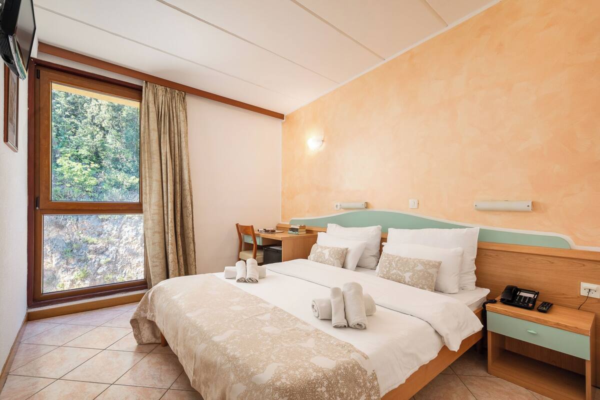 A hotel room with a bed, a desk, a chair, a nightstand, and a window with curtains.