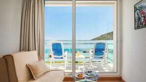 A room with a sofa, a glass table, and a view of a balcony with chairs and a table. - MASLINICA Mimosa Lido Palace Hotel (Labin)