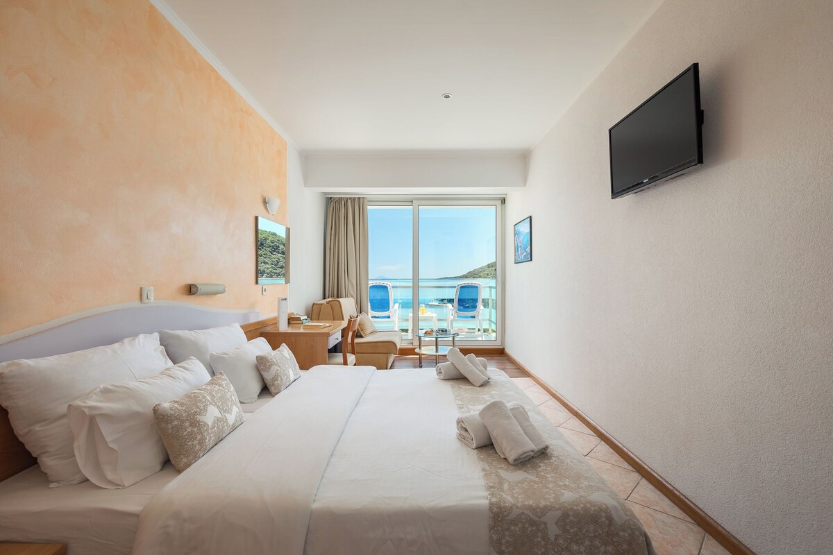 Habitación de hotel con cama, escritorio, silla, televisor y balcón con vistas.