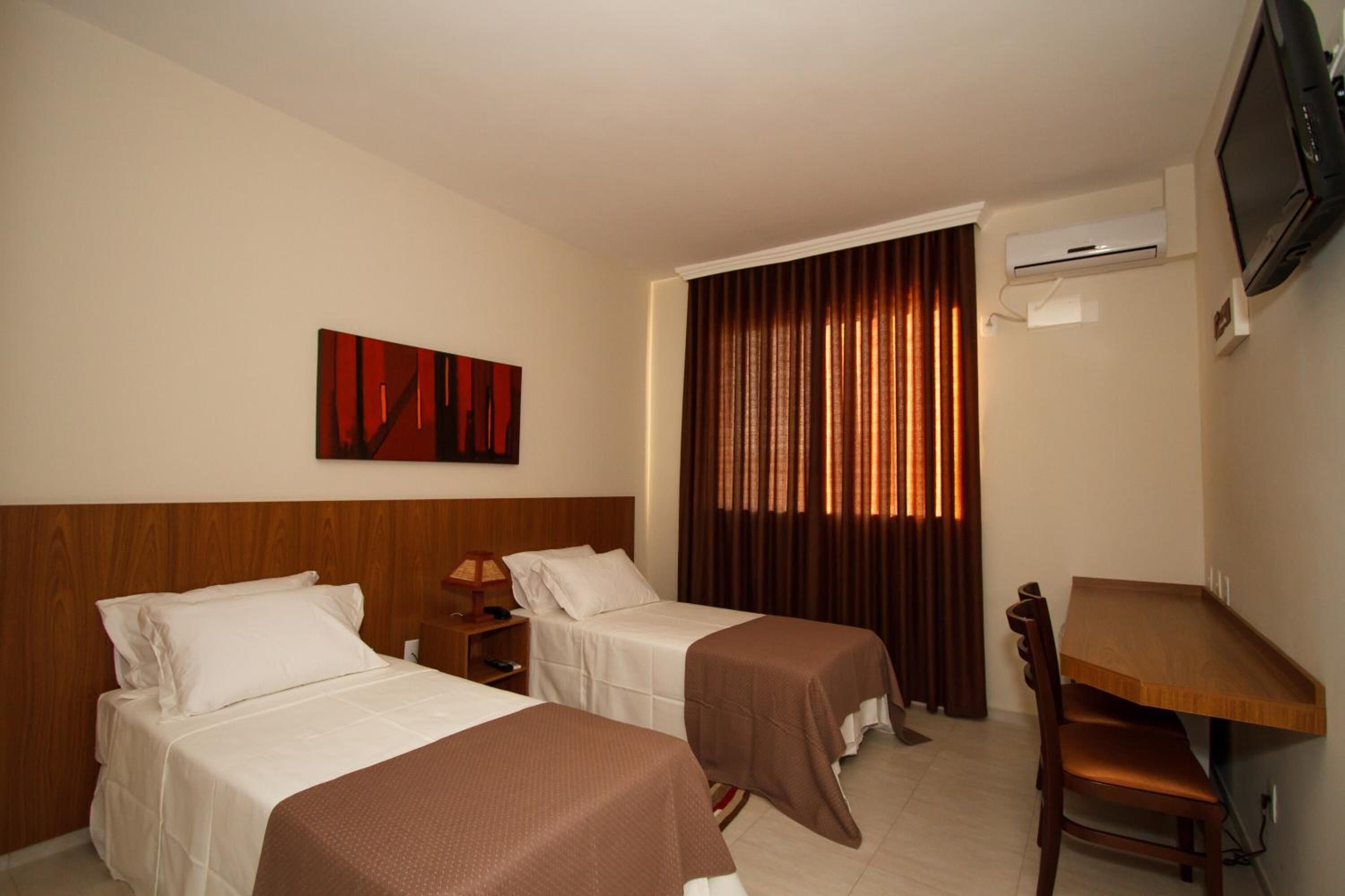 Habitación de hotel con dos camas individuales, un escritorio de madera, un televisor y un equipo de aire acondicionado.
