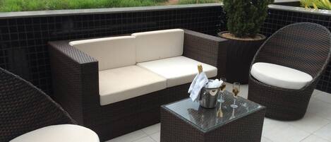 An outdoor seating area with a sofa, two chairs, and a table with drinks and a bottle.