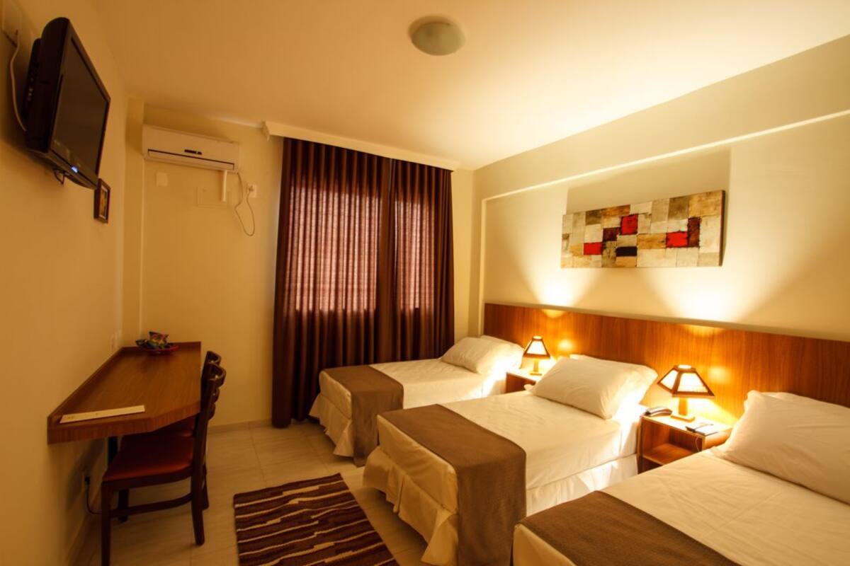 Habitación de hotel con dos camas, un escritorio, una silla, un televisor y un cuadro en la pared.