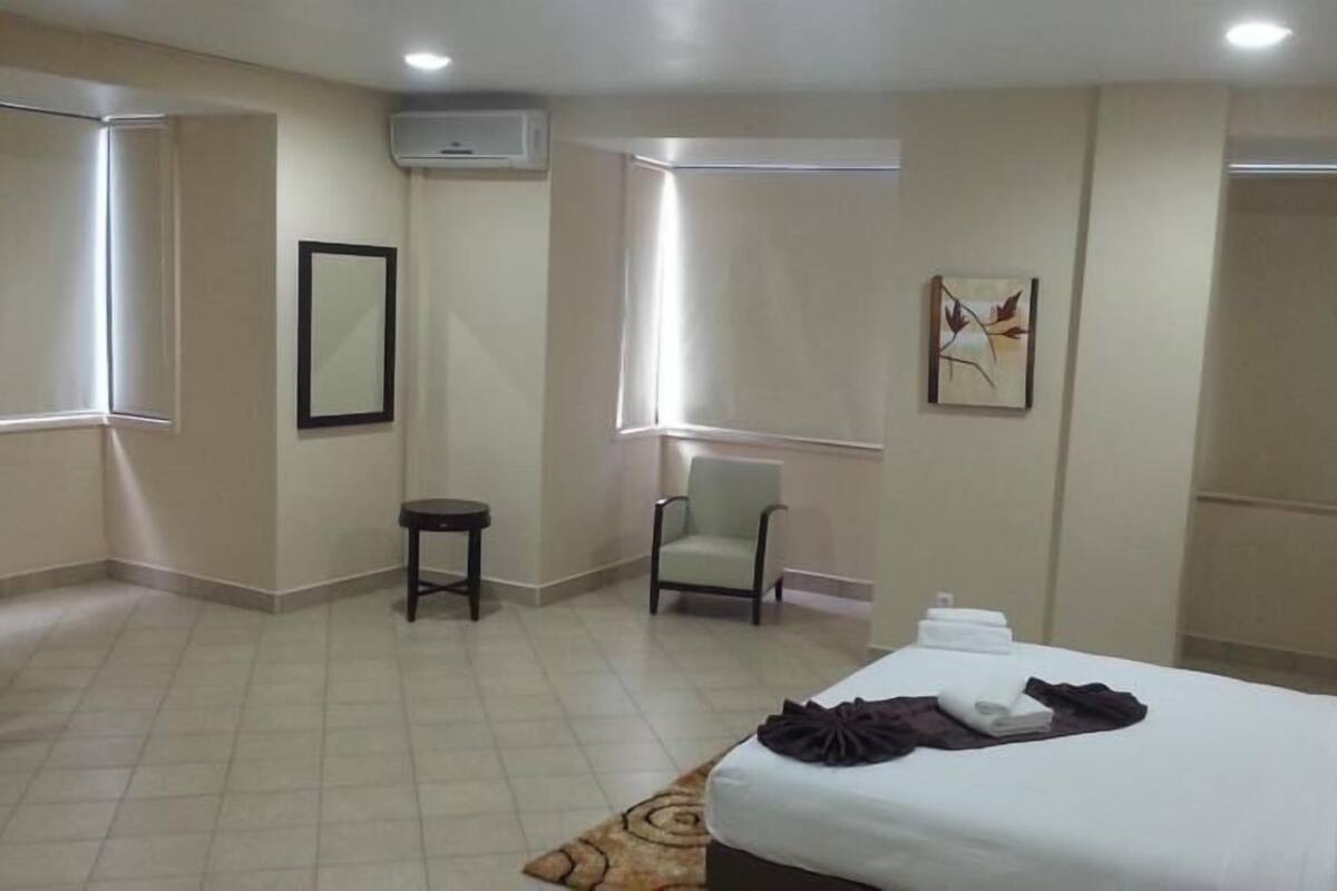 A hotel room with a bed, a chair, a small table, and a picture on the wall.
