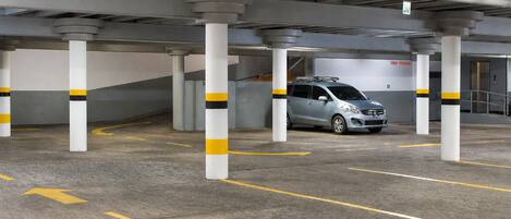 Eine Parkgarage mit Betonpfeilern, gelben Hinweisschildern und einem silbernen Auto, das in einem gekennzeichneten Parkfeld steht.