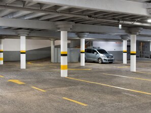 Un aparcamiento con pilares de hormigón, flechas amarillas indicando la dirección y un coche plateado estacionado en un espacio reservado.
