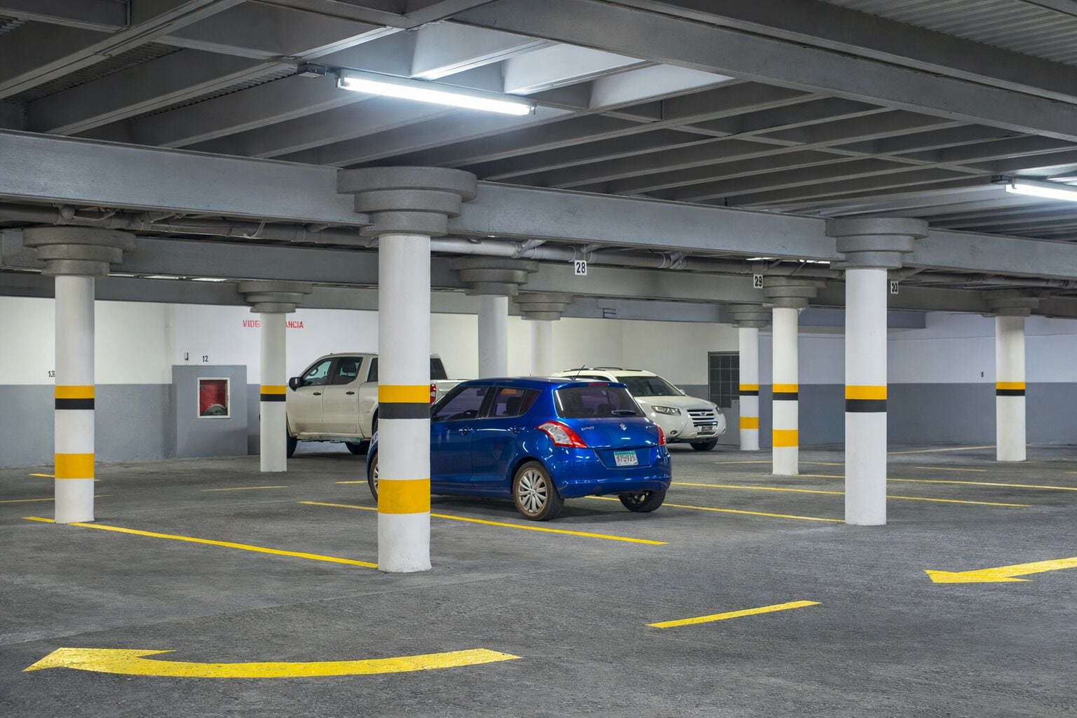 A multi-level parking garage with concrete pillars, yellow directional arrows, and a few parked cars.
