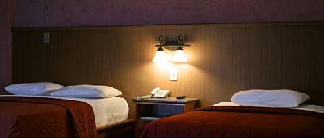 A hotel room with two beds, a nightstand with a phone, and a wall-mounted light fixture.