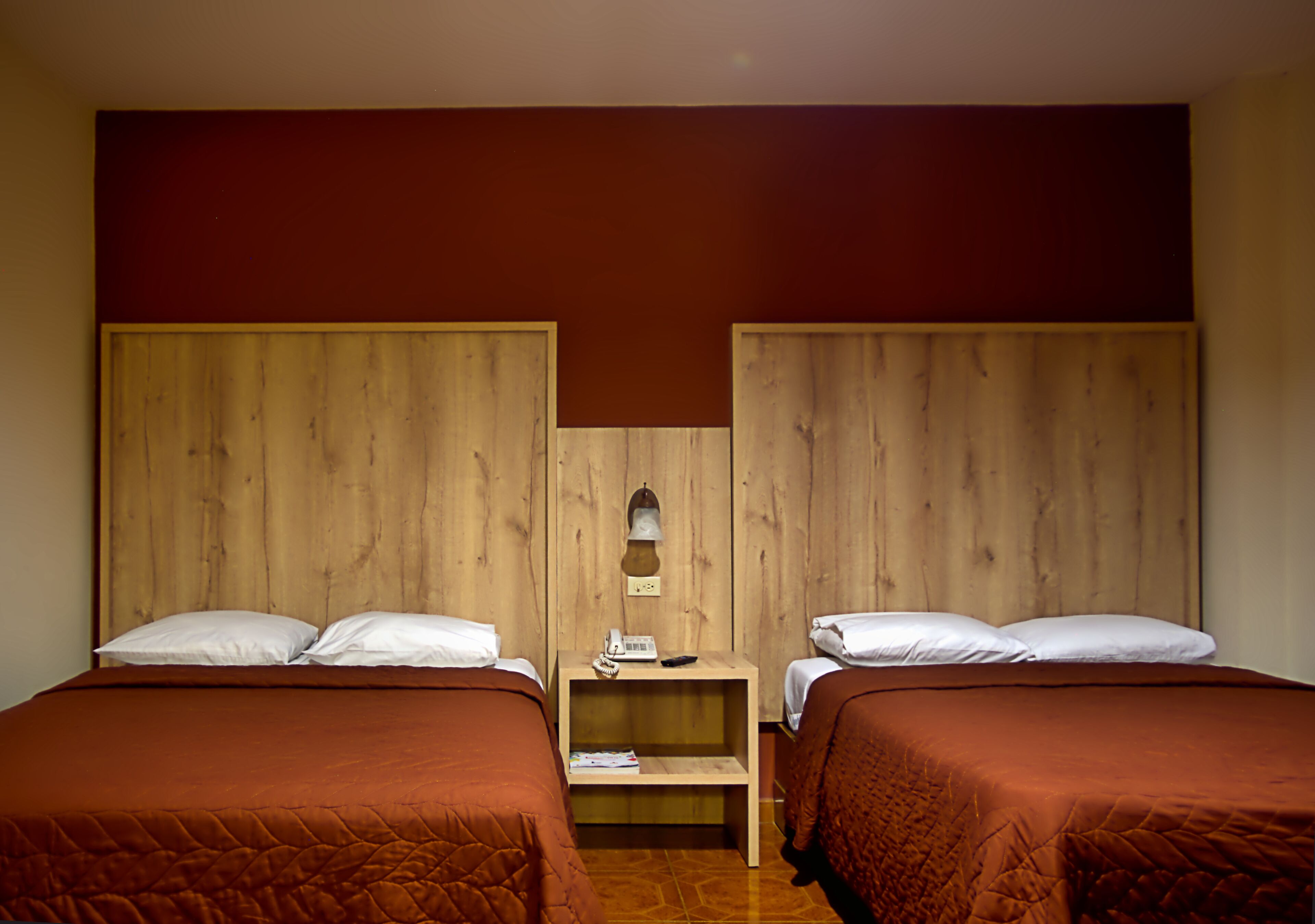 Ein Hotelzimmer mit zwei Betten, Holz-Kopfteilen, einem Nachttisch mit Lampe und einem kleinen Tisch.