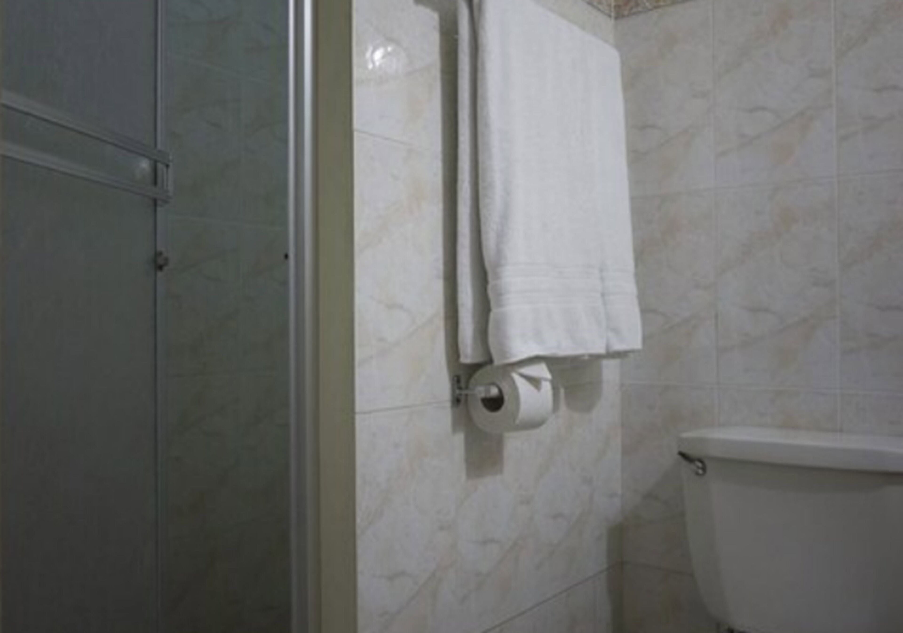A bathroom with a toilet, a towel rack with two towels, and a toilet paper holder.