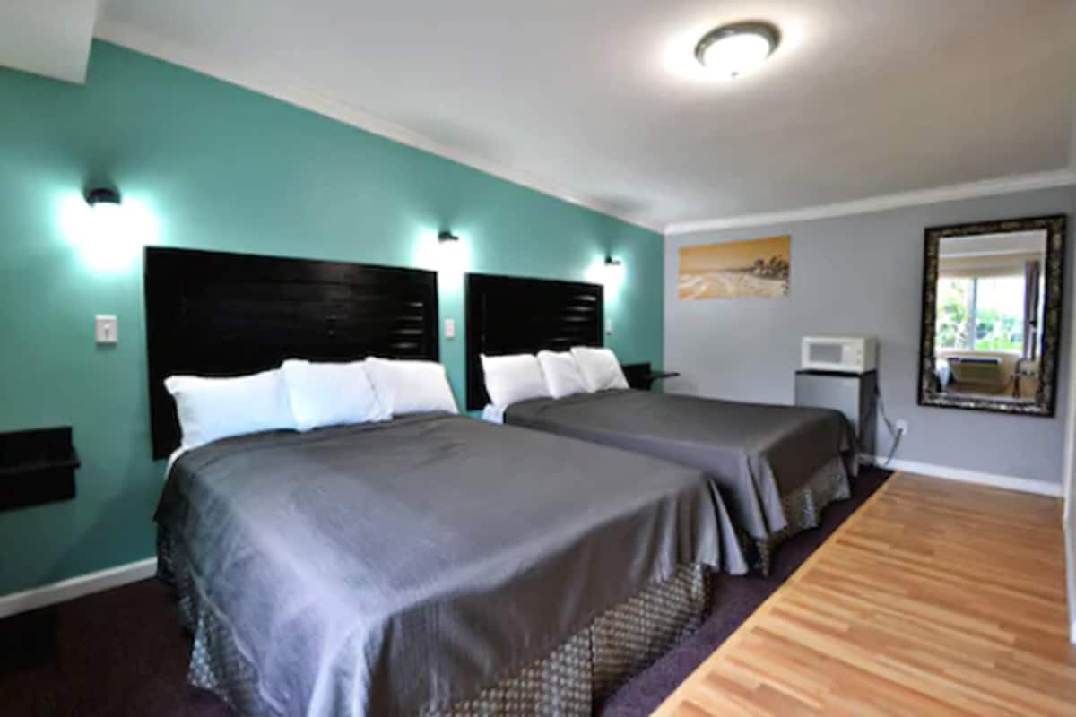 Habitación de hotel con dos camas, paredes color turquesa y piso de madera.
