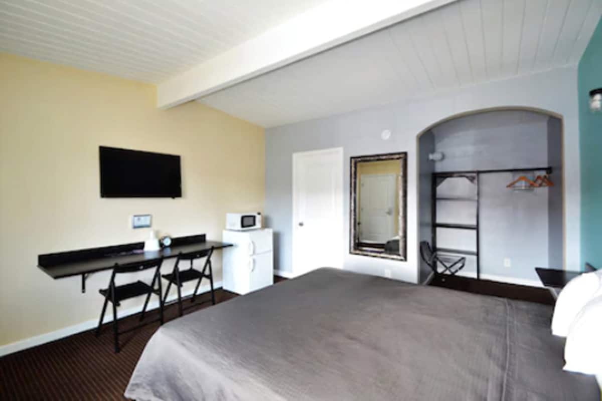Habitación de hotel con cama, escritorio, silla, televisor, microondas y armario.