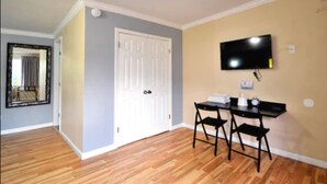 A room with a wooden floor, a white door, a flat-screen TV mounted on the wall, and a small table with two chairs. - Lodge at 32nd (San Diego)