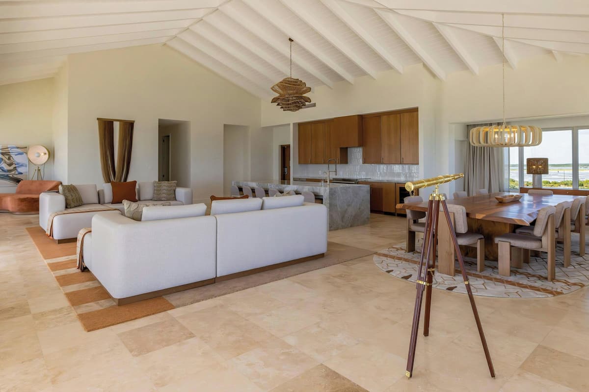 A spacious living area with a large white sofa, a dining table with chairs, and a kitchen in the background.