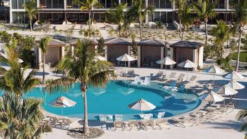 Un resort con una piscina grande rodeada de sillas de descanso y sombrillas, palmeras y un edificio moderno al fondo.