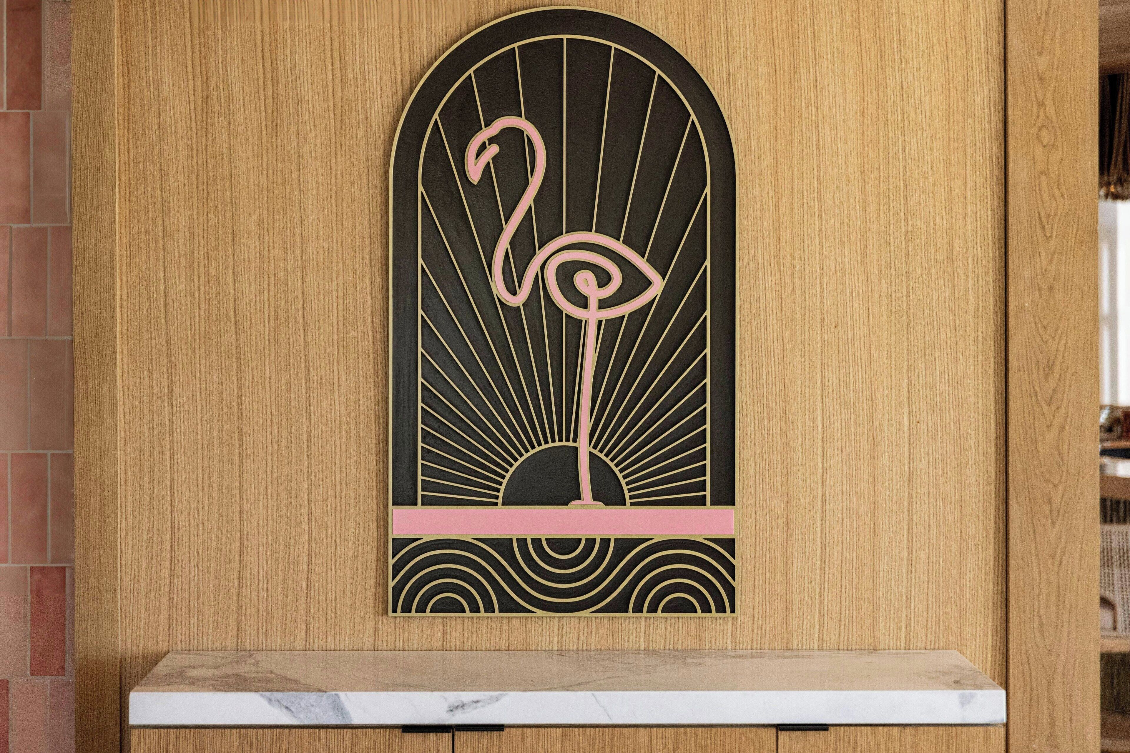 A wooden wall with a decorative panel featuring a stylized flamingo and sun design.
