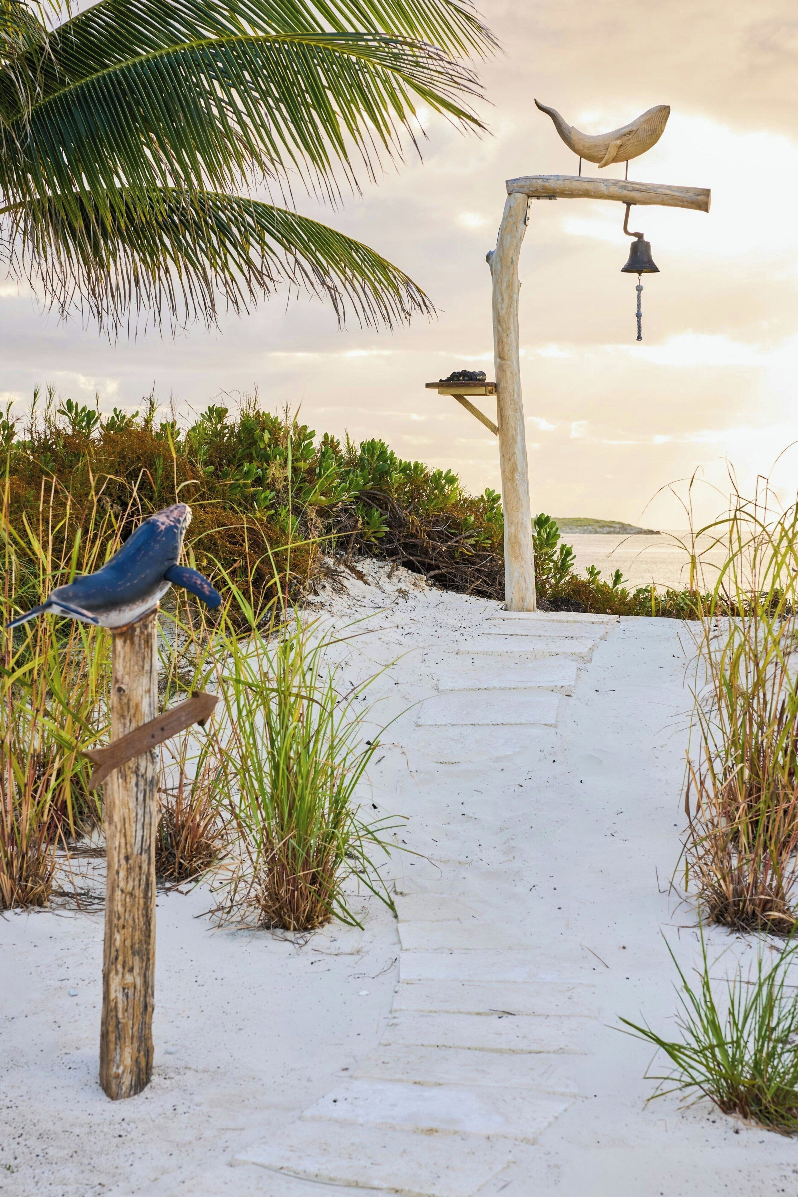 A pathway leading through a sandy area with a wooden post and a bird sculpture.