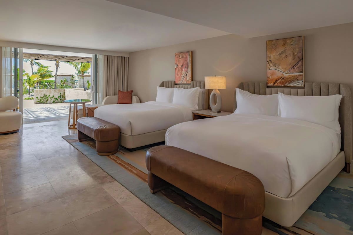 A hotel room with two beds, a sofa, a small table, and a view of the outdoors.
