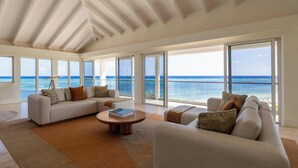 Amplio salón con un gran ventanal con vistas al mar, techo blanco y diseño interior moderno.