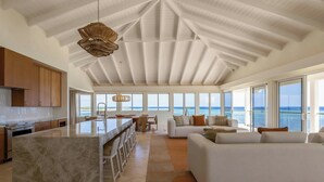 Amplia sala de estar con un ventanal con vistas al océano, una cocina con armarios de madera y una isla central.
