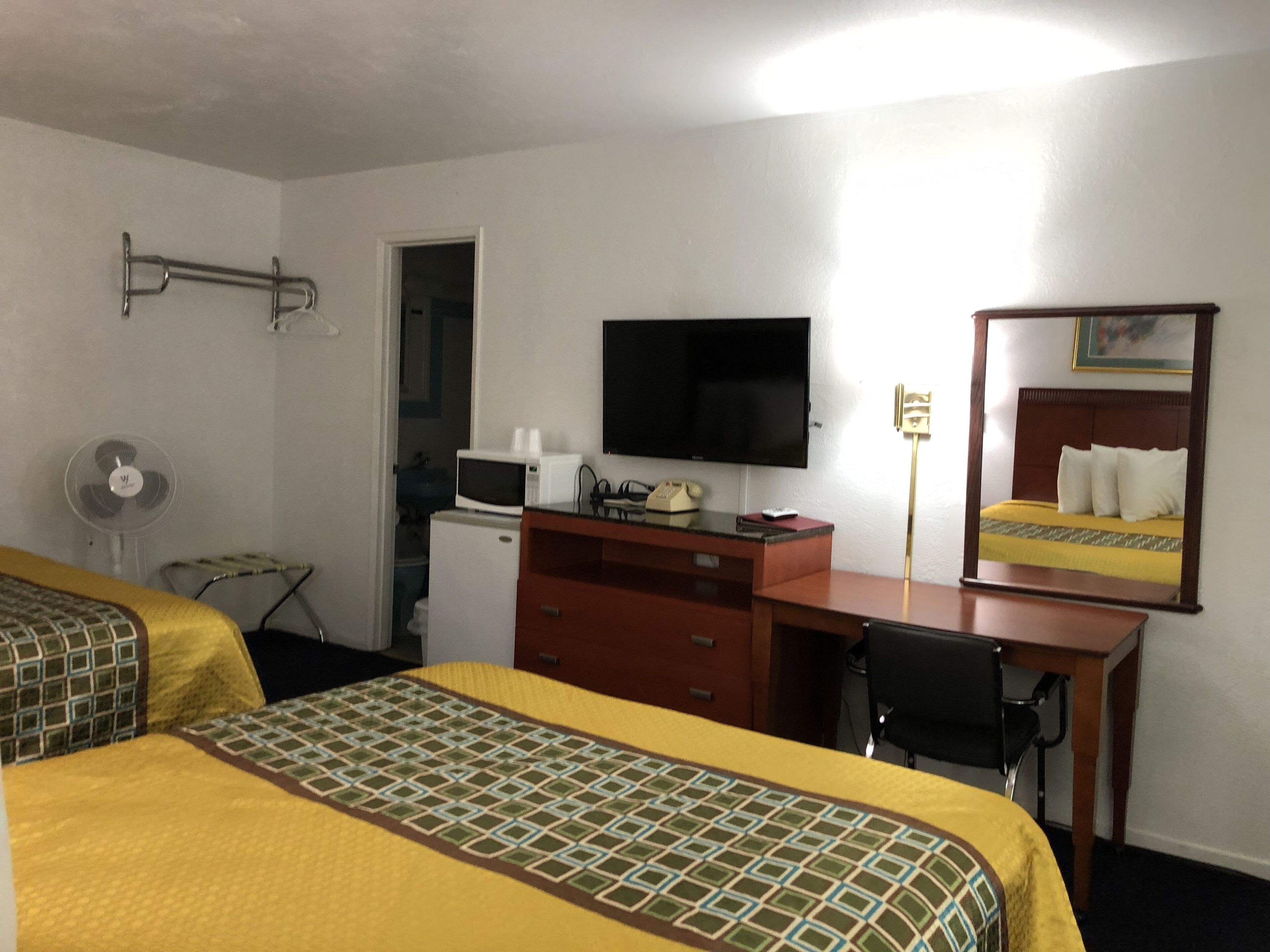 A hotel room with two beds, a desk, a television, a mirror, a fan, and a microwave.