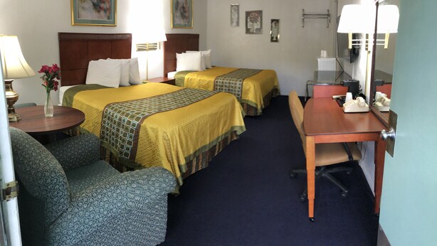 A hotel room with two beds, a desk, a chair, a lamp, a vase with flowers, and a mirror.