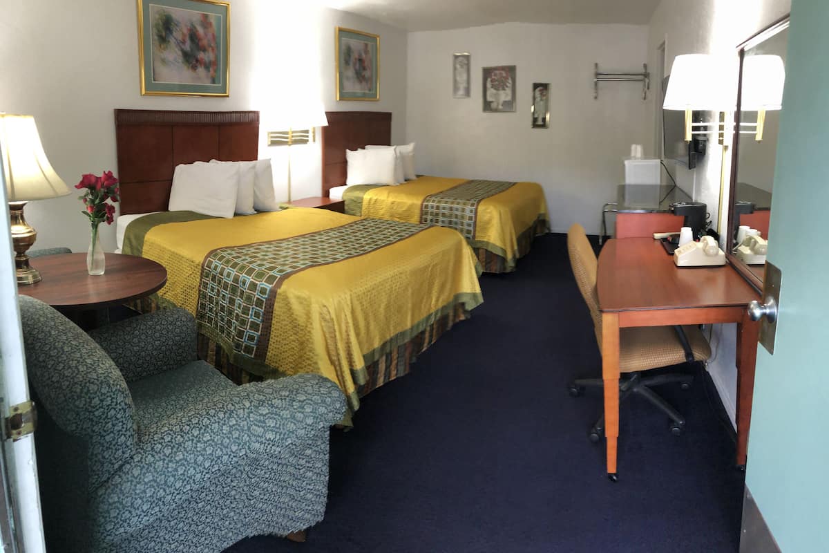 A hotel room with two beds, a desk, a chair, a lamp, a vase with flowers, and a mirror.