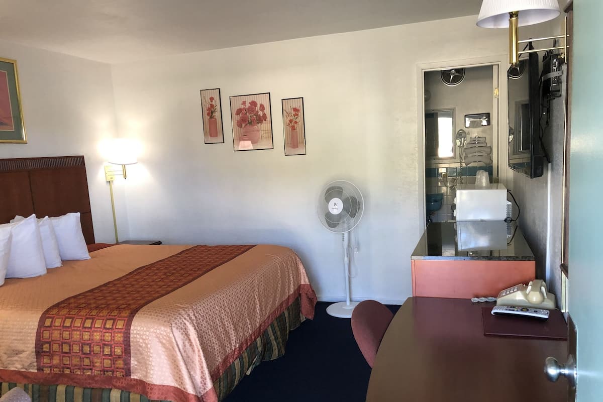 A hotel room with a bed, bedside table, lamp, fan, and a mirror.
