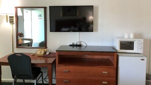 A hotel room with a desk, chair, television, microwave, and a small refrigerator.