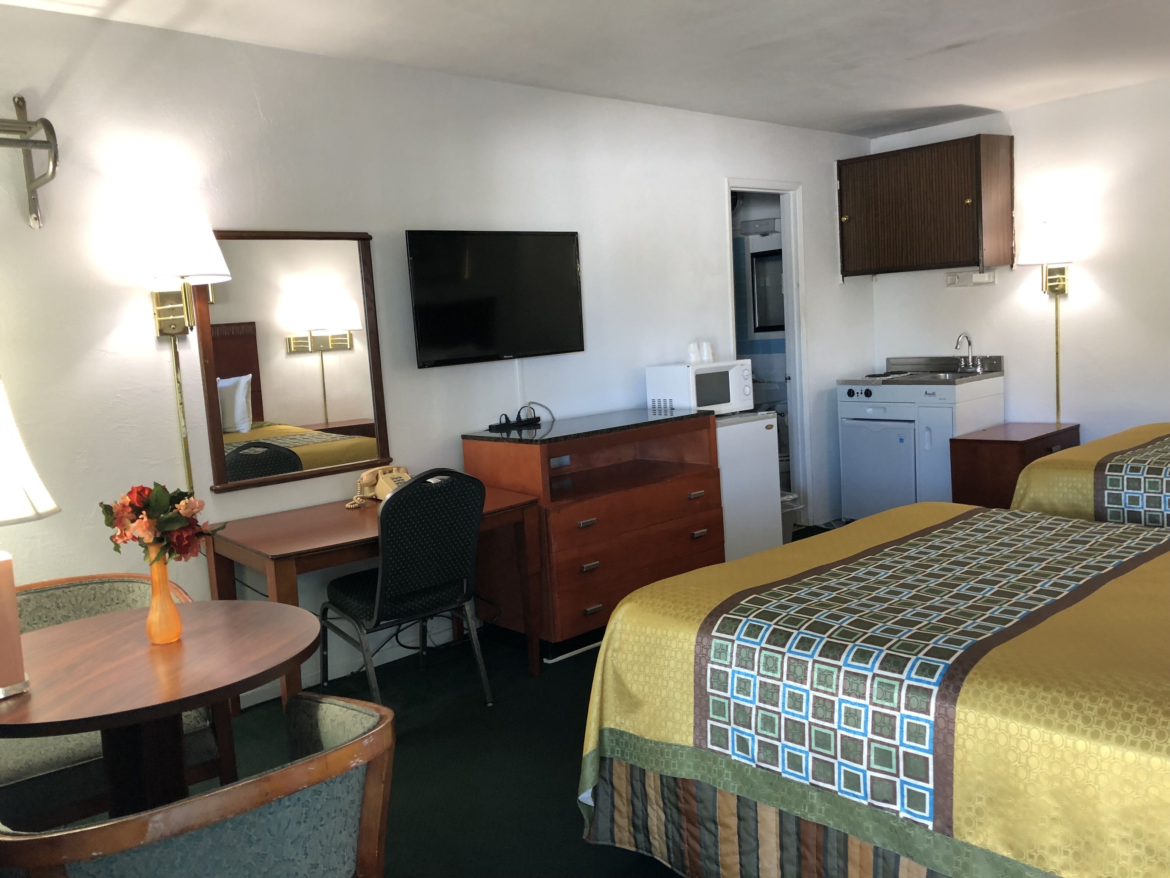 A hotel room with a desk, chair, bed, TV, kitchenette, and a bathroom visible through an open door.