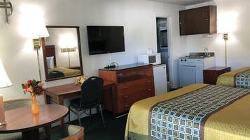 A hotel room with a desk, chair, bed, TV, kitchenette, and a bathroom visible through an open door.