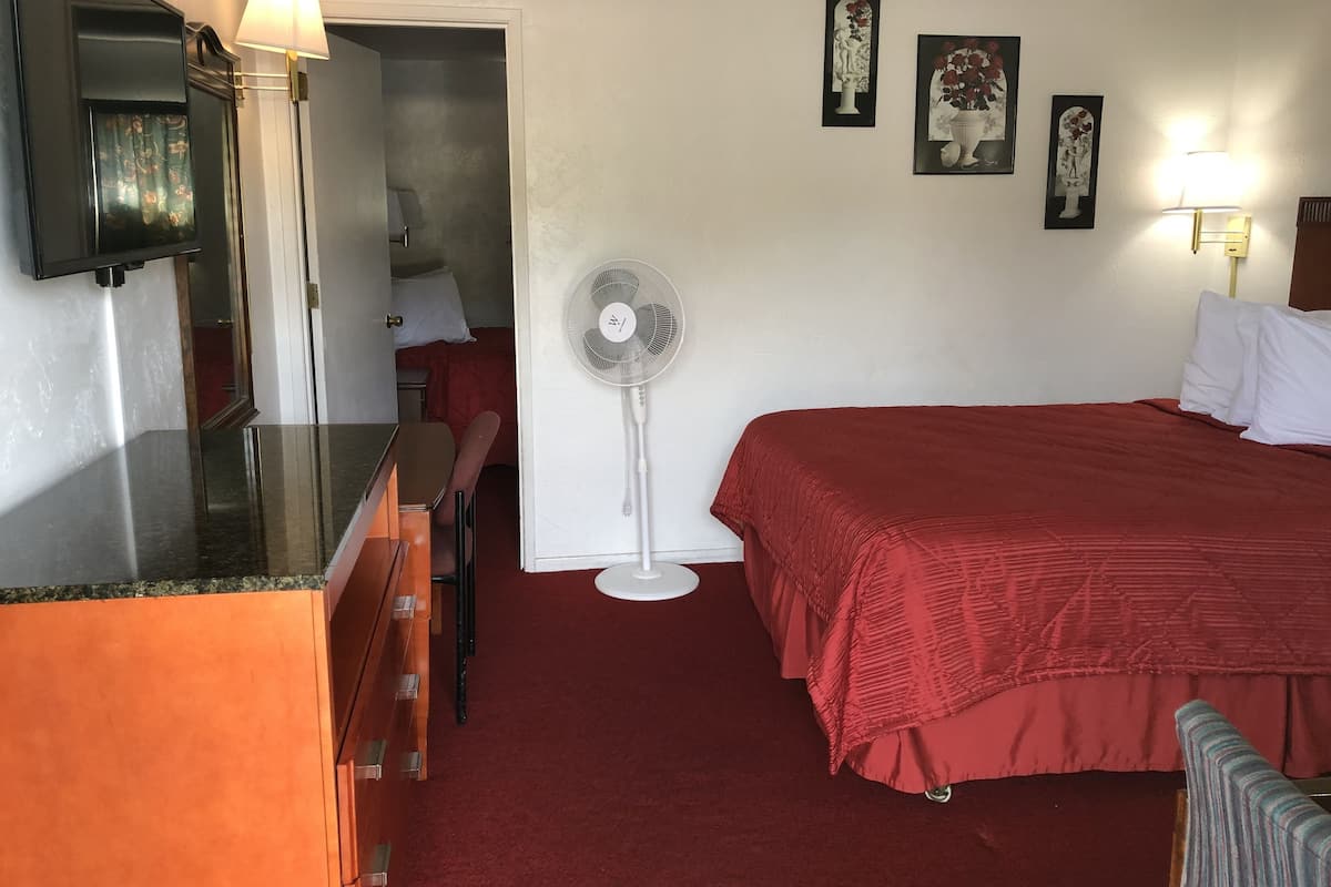A hotel room with a bed, a desk, a chair, a fan, and wall-mounted artwork.