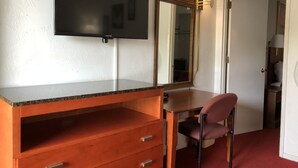 A room with a wooden dresser, a flat-screen TV mounted above it, a mirror, a chair, and a door leading to another room.