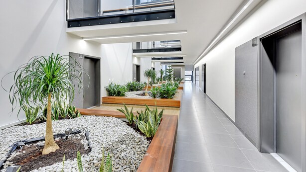 A modern interior with a central garden, a mezzanine level, and a long corridor with doors. - Apartinfo Apartments - Sadowa (Gdansk)