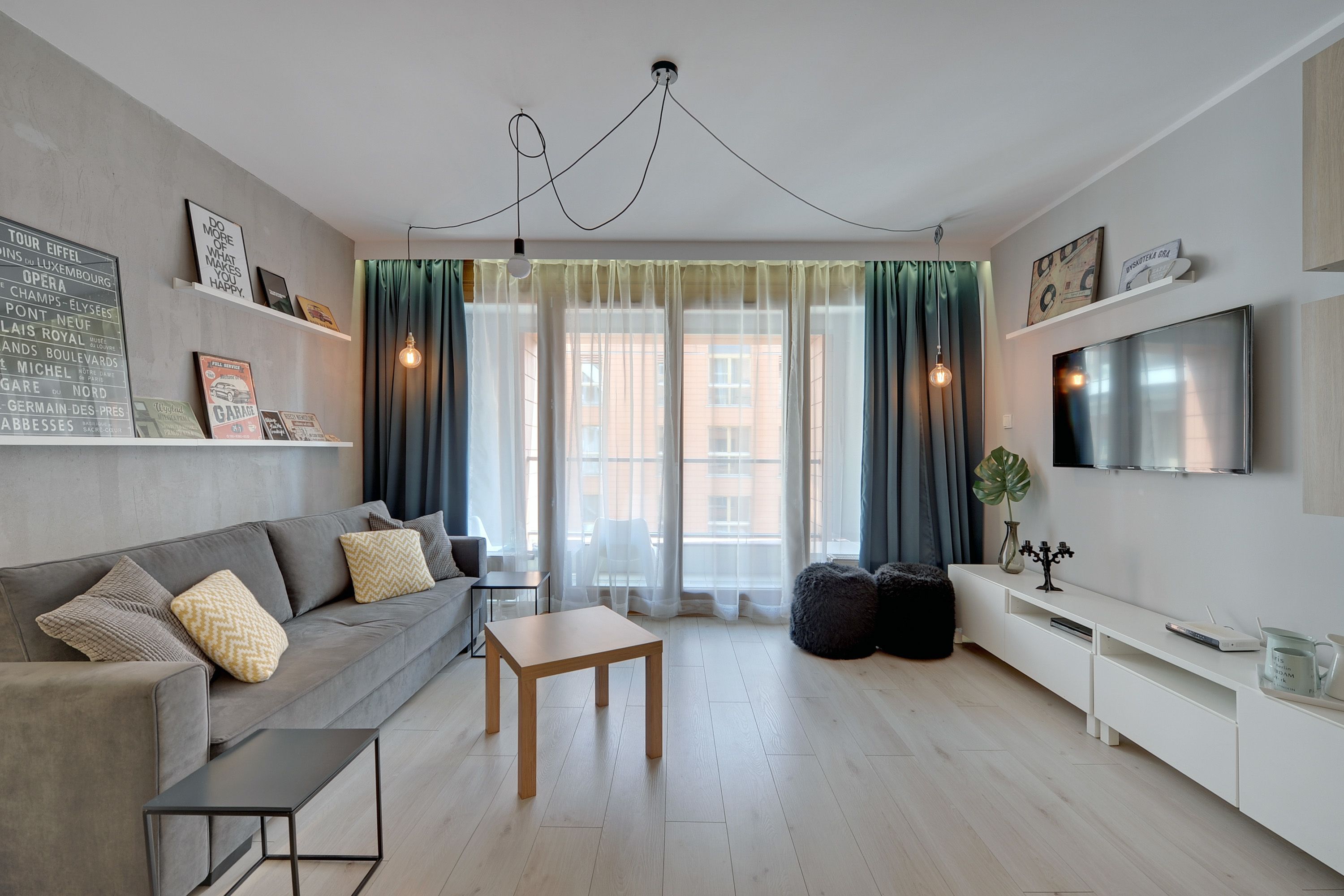 A modern living room with a grey sofa, a wooden coffee table, and a TV on a white stand.