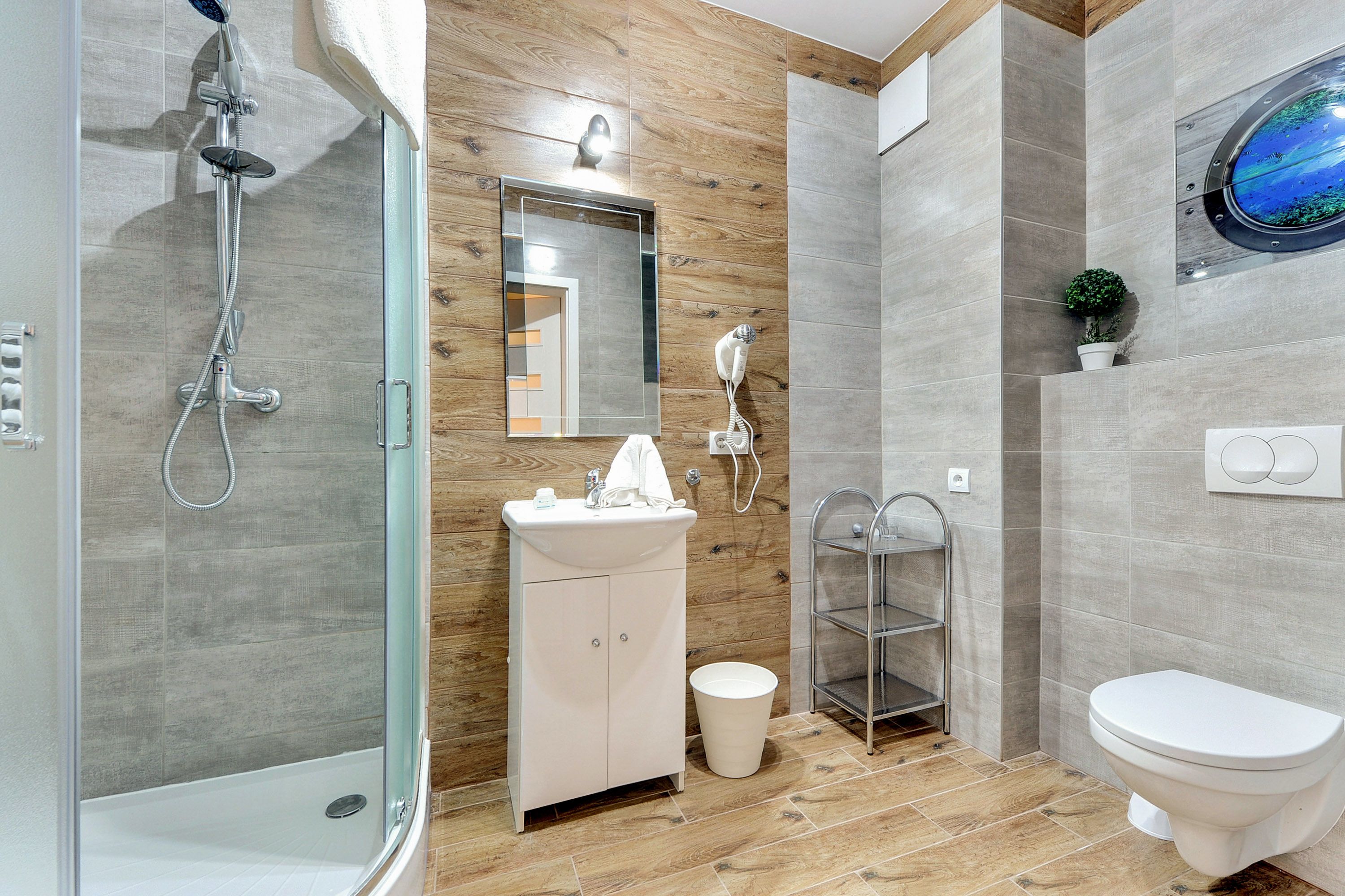 A modern bathroom with a glass-enclosed shower, a white sink, a mirror, a towel rack, a toilet, and a small potted plant.
