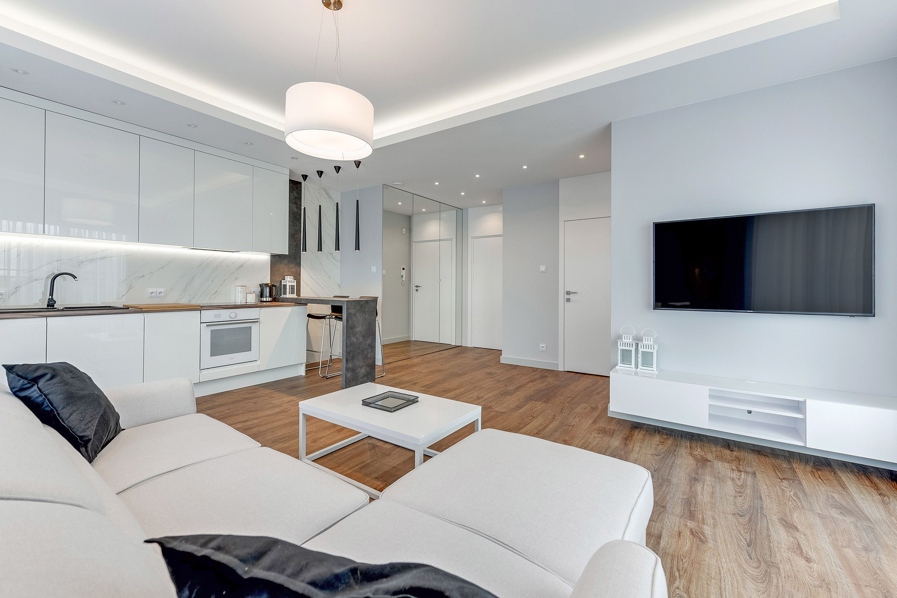 A modern living room with a white sofa, a coffee table, and a TV mounted on the wall.