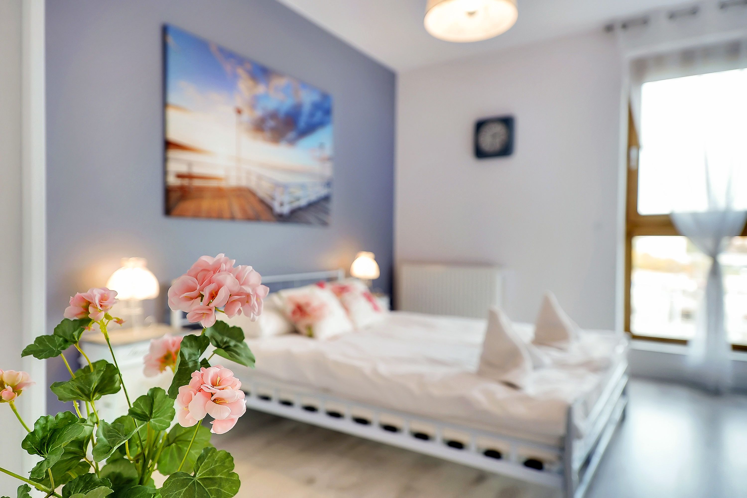 A bedroom with a bed, bedside lamps, a painting on the wall, and a window.