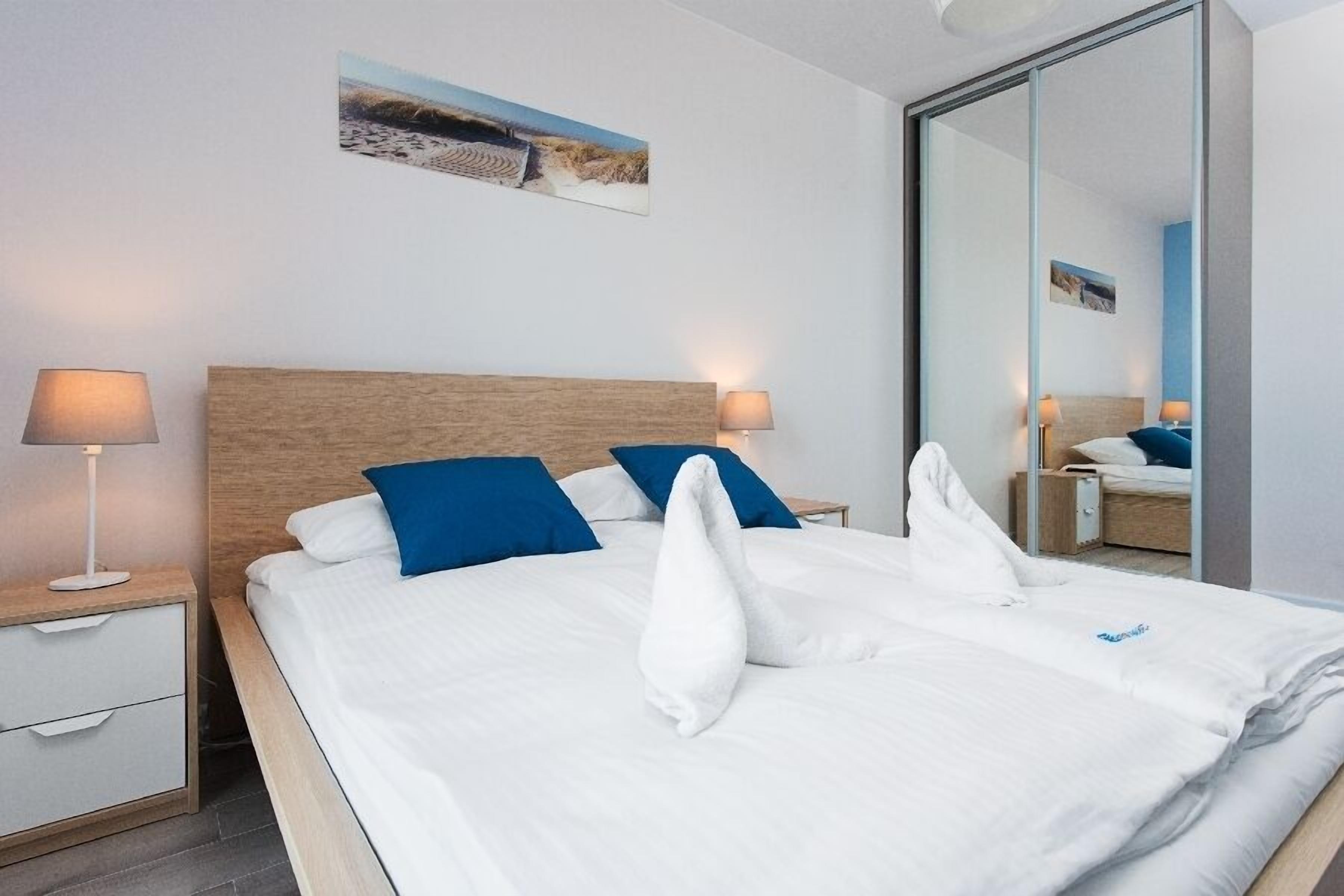 A neatly made bed with white and blue pillows, a wooden headboard, and a nightstand with a lamp.