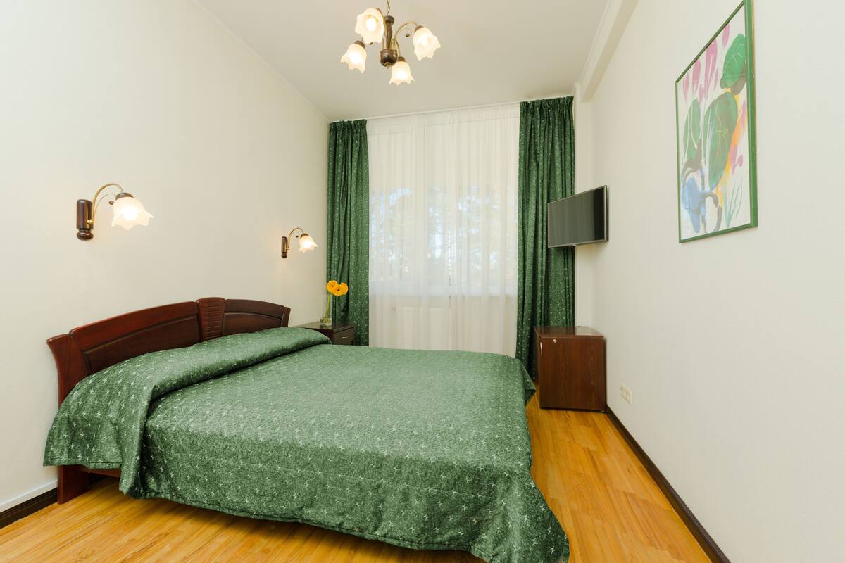 Quarto bem arrumado com cama de madeira, cortinas verdes, televisão de tela plana e um quadro na parede.