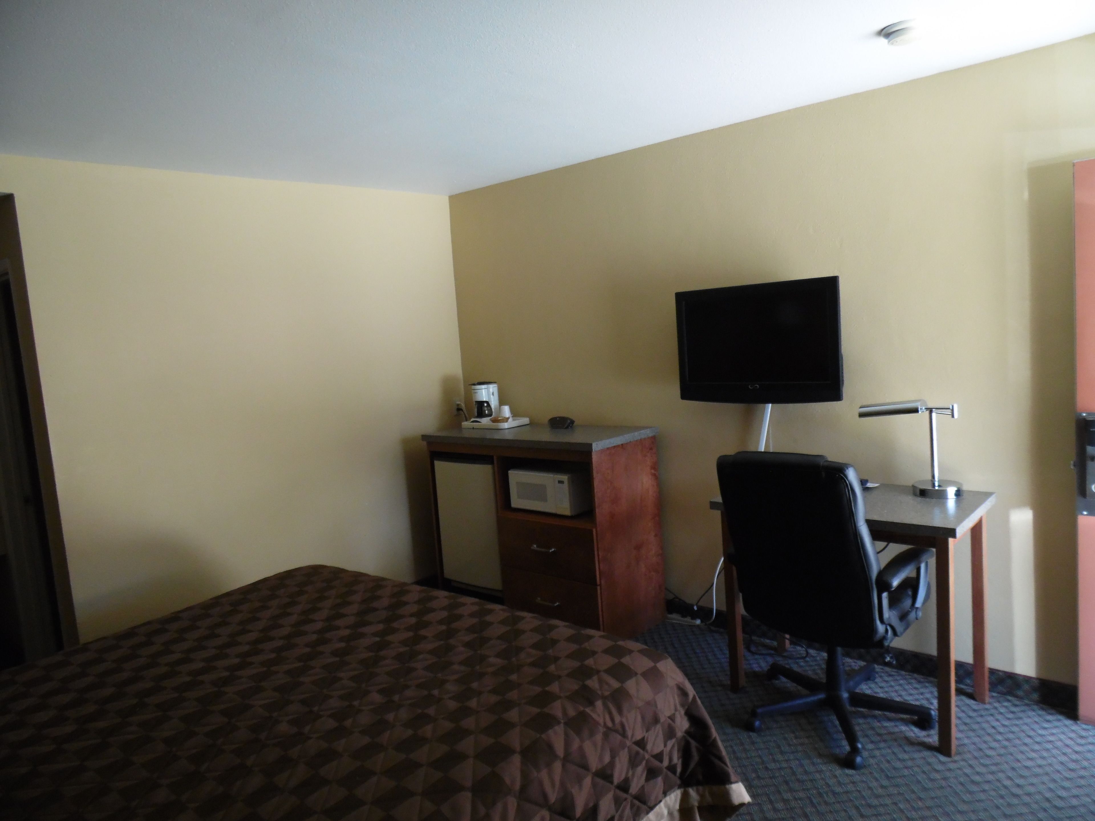 A hotel room with a bed, a desk with a computer and a flat-screen TV, and a coffee maker.